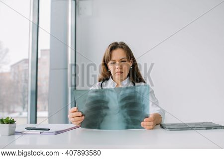 Young Caucasian Woman Doctor Wearing White Medical Coat And Stethoscope Holds The X-ray. Medicine Co