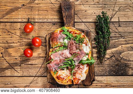 Sliced Pizza With Prosciutto Parma Ham, Arugula And Parmesan Cheese On A Wooden Board. Wooden Backgr