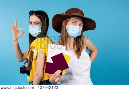 Two Female Travelers In Medical Protective Masks, Holding Tickets And Passports, Standing Back To Ba