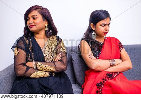 Two Young Indian Women In Traditional Sari And Bindi Looking In Different Sides In Interior Of Livin