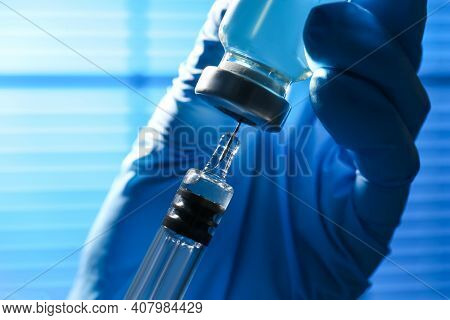 Woman Filling Syringe With Vaccine From Vial On Blurred Background, Closeup