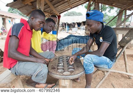 Anekro, Ivory Coast - 27 August 2015: Young Playing The Awalé Under A Shed In The Village. Four Youn