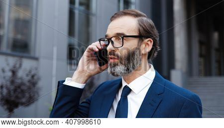 Caucasian Middle-aged Man In Glasses Talking On Mobile Phone And Drinking Coffe To-go In Morning Out