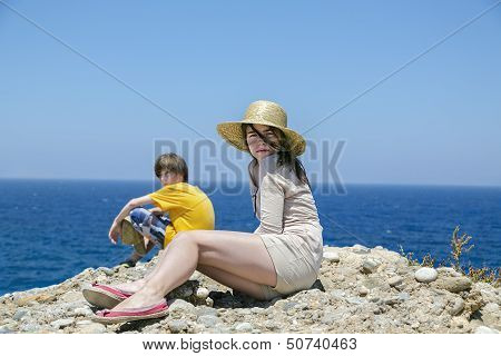 Two Teens Sitting On The Top Of A Mountain With Blue Ocean In Background