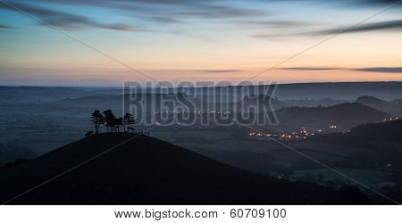 Beautiful Sunrise Dawn Landscape Of Hills Overlooking Brightly Lit Town In Valley Below