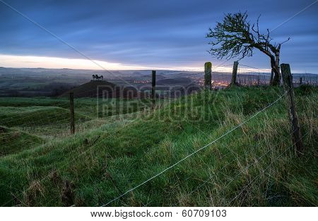 Beautiful Sunrise Dawn Landscape Of Hills Overlooking Brightly Lit Town In Valley Below