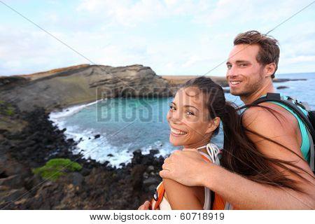Hiking - travel couple tourist on Hawaii hike. Tourist backpackers walking on Green Sand Beach, Papakolea on Big Island, Hawaii, USA. Interracial young happy couple traveling with backpacks.