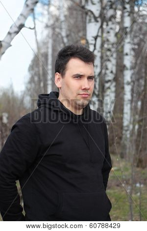 Young Man Dressed In Black Stands In Spring Forest And Looks Aside