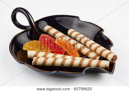 cookie in form tubes with fruit jellies on a black saucer