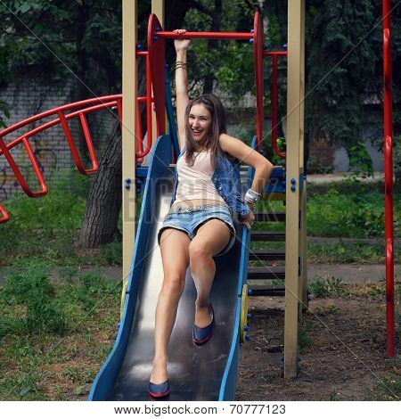 Happy teen girl has fun  on child hillock on playground. Outdoors. Image toned and noise added.