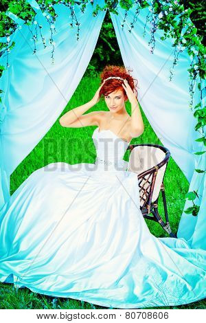 Beautiful bride with chaming red hair sitting under the wedding arch. Wedding dress and accessories. Wedding decoration. 