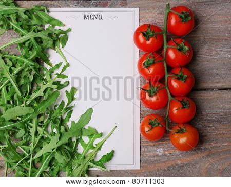 Menu sheet of paper with cherry tomatoes and arugula on rustic wooden surface background
