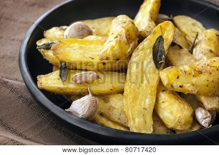 Roasted fingerling or kipfler potatoes, with sage leaves, in black dish.