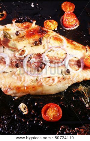 Dish of Pangasius fillet with onion and cherry tomatoes on burn pan background
