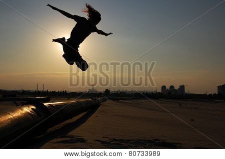 Man jumps over the pipe in backlight on the dawn of the day