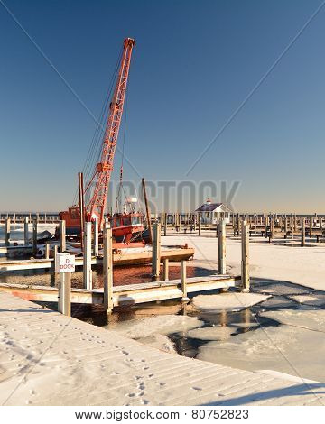 repair barge with crane in empty public marina in winter with animal tracks on dock