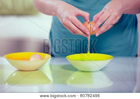 Female hands separating yolk and white of a cracked egg