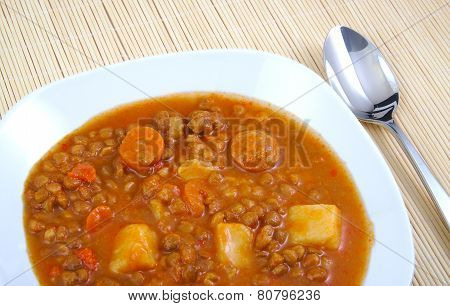 Brown cooked lentils with sausage, carrot and potato with metal spoon
