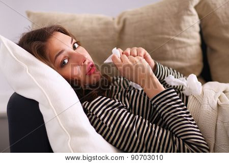 Portrait of a sick woman blowing her nose while sitting on the sofa