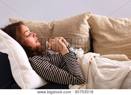 Portrait of a sick woman blowing her nose while sitting on the sofa