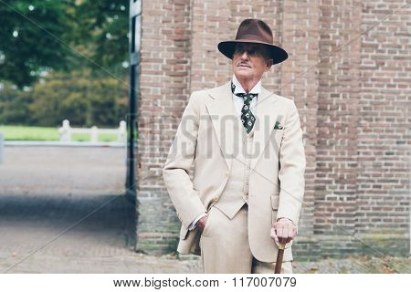 Senior Dandy Standing With Cane In Front Of Gate.