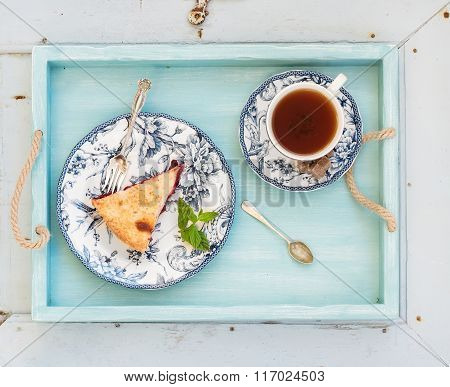 Piece of double crust plum pie and black tea in vintage porcelain cup, blue wooden tray. Top view, h
