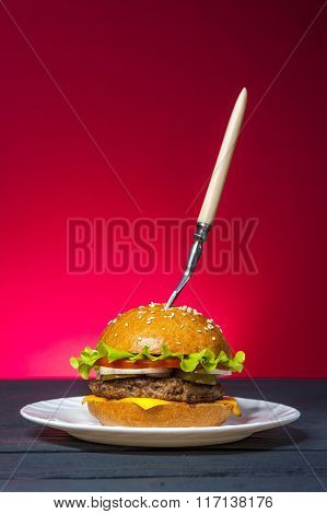 Hamburger with vegetables on white plate with fork on wooden table.