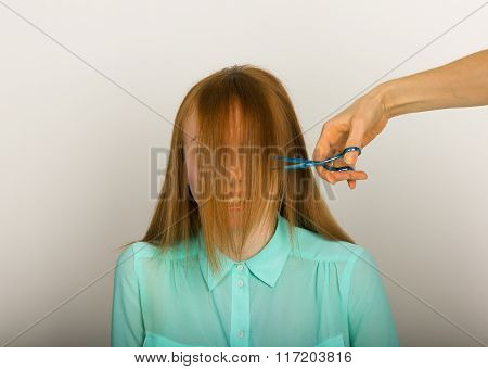 Beautiful young red-haired girl at the hairdresser makes blow drying, shorn bangs, hair polishing