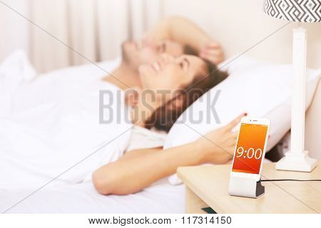 Young couple waking up with mobile alarm clock