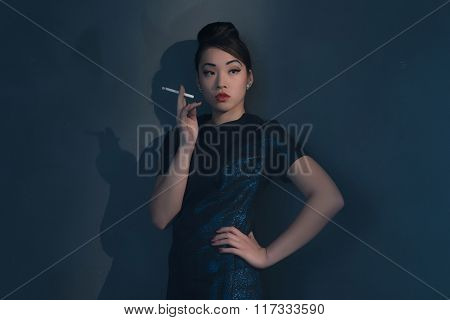 Retro 40S Styled Asian Woman In Evening Dress Smoking Cigarette. Leaning Against Wall.