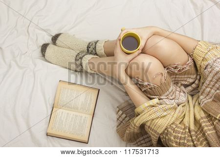 Woman on the bed with old book and cup of coffee in hands, top view point. Copy space for text. Soft