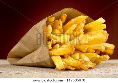 French Fries In The Paper Bag On Burned Background On Wooden Table