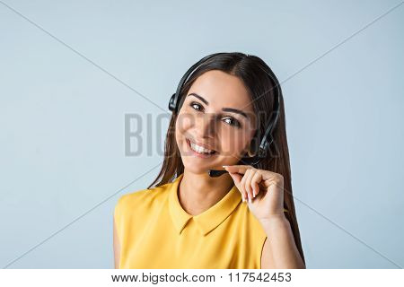 Photo of beautiful young call center operator standing near gray background. Woman with headphones looking at camera and smiling