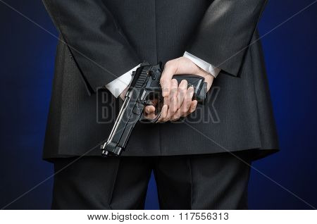 Firearms And Security Topic: A Man In A Black Suit Holding A Gun On A Dark Blue Background In Studio