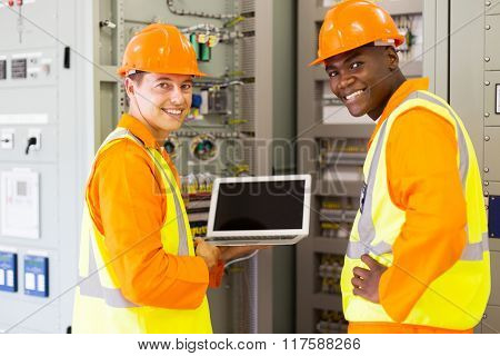 happy electrical co-workers using laptop computer checking transformer control box