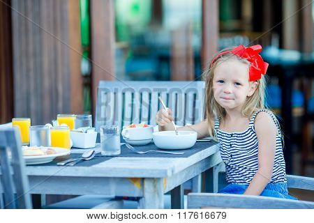 Adorable little girl having breakfast at outdoor cafe