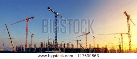Industrial Landscape With Silhouettes Of Cranes On The Sunset Background. Construction Of Stadium