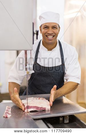portrait of cheerful mature male butcher cutting meat on bandsaw