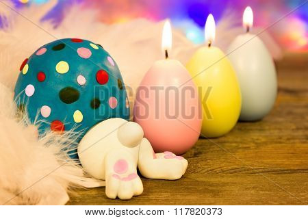 A bunny slips into a colorful Easter egg next to burning candles