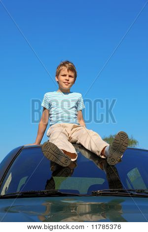 Pojken sitter på taket av bilen, blå himmel