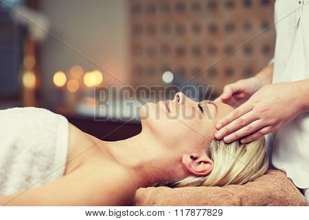 people, beauty, spa, healthy lifestyle and relaxation concept - close up of beautiful young woman lying with closed eyes and having face or head massage in spa