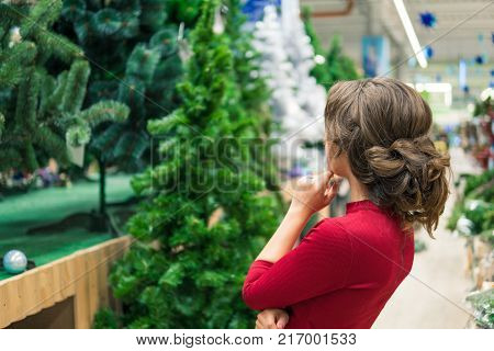 View from behind. Cheerful happy customer girl choosing Christmas tree for the new year on Christmas Eve. difficult decision. Various choice