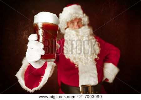 Portrait of Man in Santa Claus Costume - with a Luxurious White Beard, Santa's Hat and a Red Costume at red studio background with beer