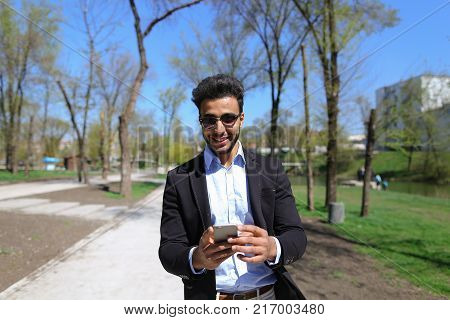 Man hold phone in hand and talking with mom. Son has dimple on cheeks, beard, short hair and long nose. Person dressed in black jacket and blue shirt. Concept of new apps modern technologies and long talks and cheep tariff plans.