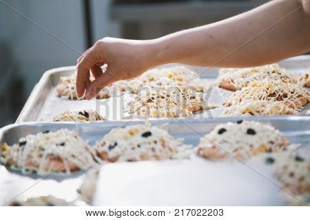 Cook puts the filling on the mini pizza in the bakery close-up