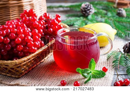 Tea from fresh red viburnum in a transparent glass on a wooden background near branch with red berries of viburnum on a table