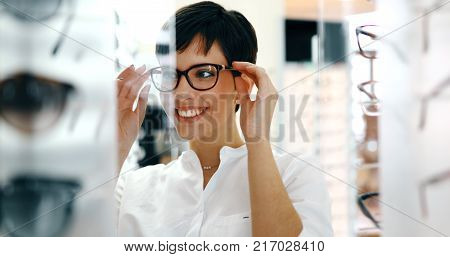 Beautiful woman with optician trying eyeglasses at optics store