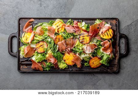 Lettuce, ham serrano and grilled peaches salad served on black board. Top view.