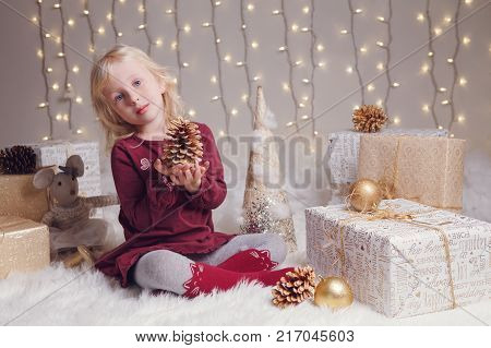Portrait of white blonde Caucasian child girl with blue eyes sitting on floor with toys celebrating Christmas or New Year holiday.