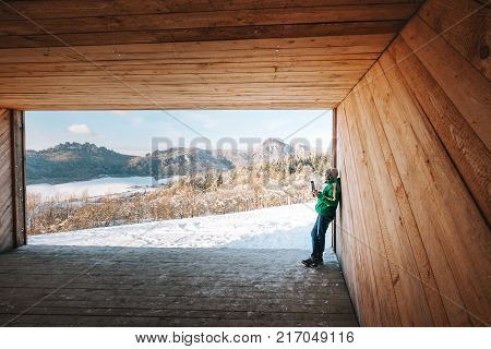 Man drinks a hot drink in wooden hangar with mountains panorama view